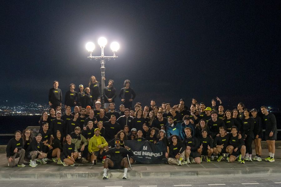 The whole LACE group in black long sleeves under a street lamp on the Naples seafront at night, holding the LACE Napoli banner